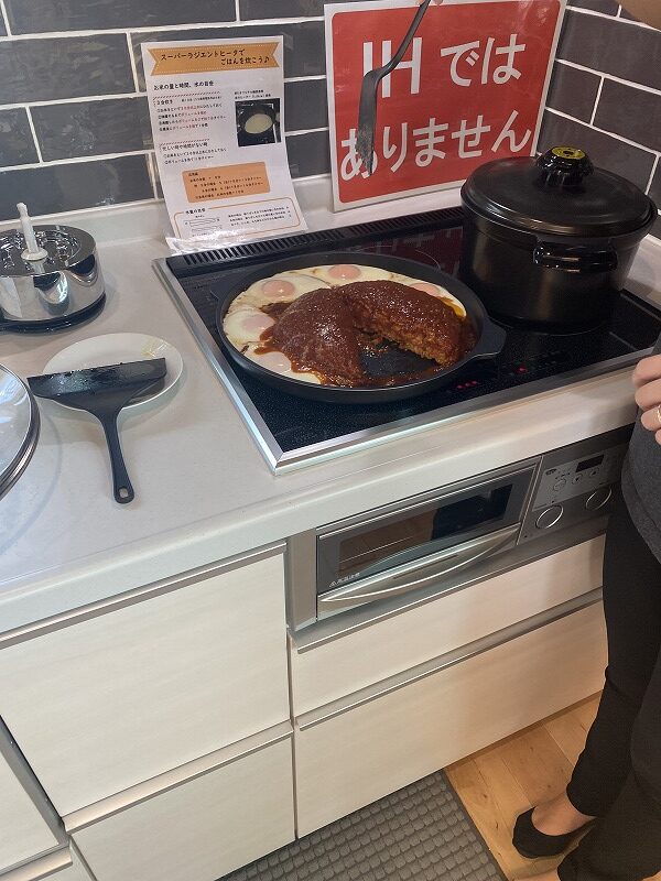 建築工房いろはの注文住宅のキッチンで、スーパーラジェントヒーターに並んだ調理中のハンバーグと目玉焼き、周囲の調理器具や収納の様子を捉えた写真で、家づくりや住宅会社選びの参考となる設備環境。