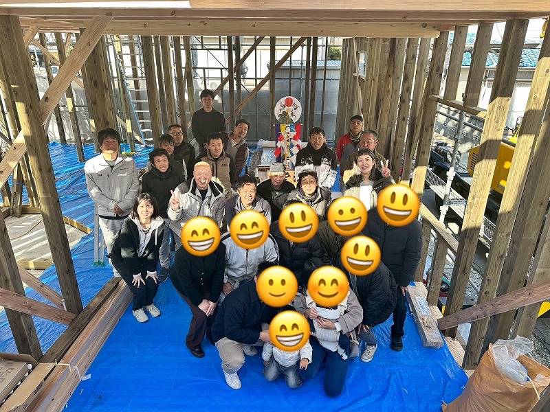 建築工房いろはによる注文住宅の建築現場で、上棟式に参加した家族や関係者が木造構造内で記念撮影を行う様子を写した写真。
