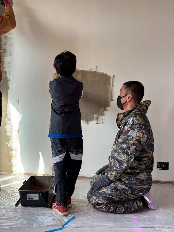 建築工房いろはの注文住宅現場で、塗装職人が洋風漆喰の壁塗りを子どもに教える家づくりの一場面を撮影した写真。