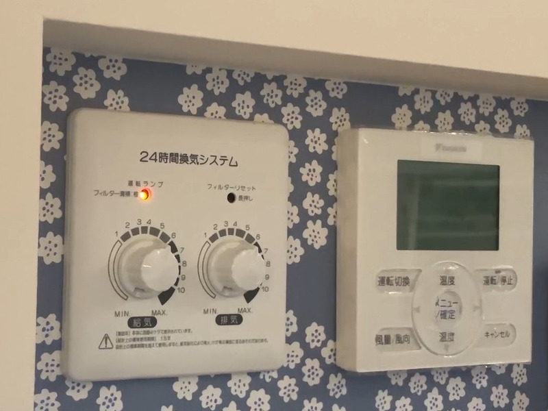 ALTテキスト（社名オプション：建築工房いろは）：
建築工房いろはが家づくりや注文住宅のメンテナンスとして、室内壁に設置された24時間換気システムと空調リモコンの操作パネルを記録した写真で、お手入れ前のランプの状態を客観的に示す内容。