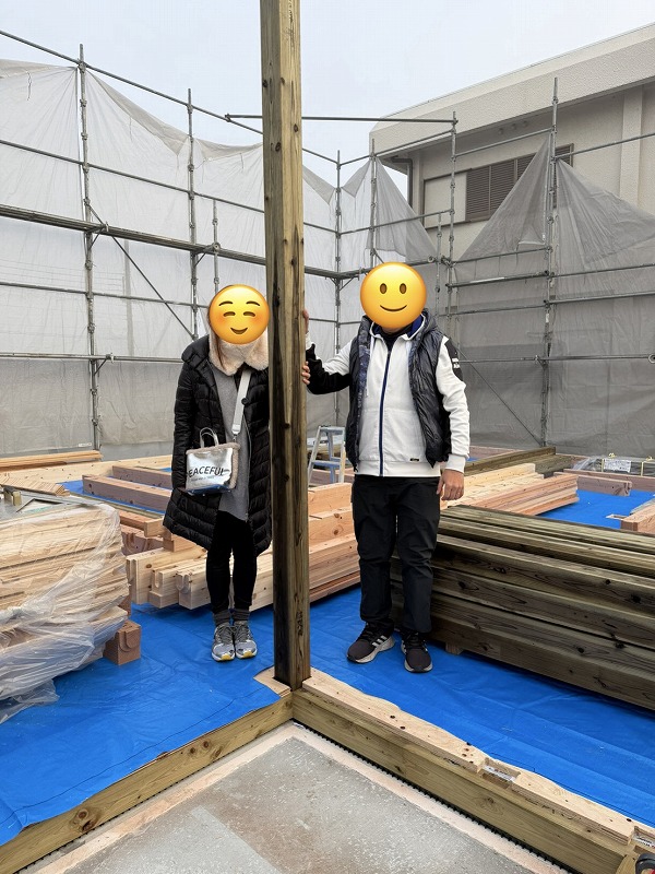 建築工房いろはによる注文住宅の上棟現場で、冬装備の施主が柱の前に立ち家づくりの節目を記念している。