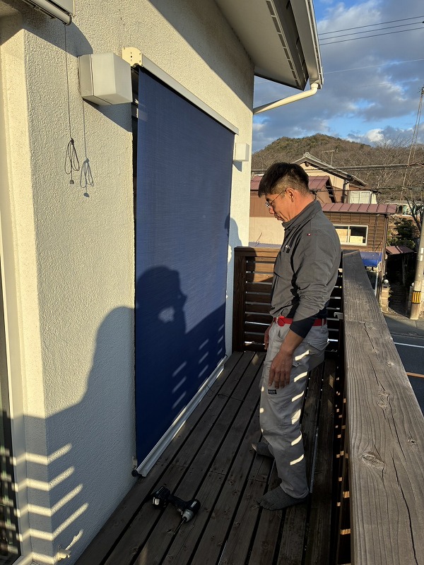 バルコニーで男性がアウターシェードの受け材を確認している様子を写した写真で、建築工房いろはが行う注文住宅の家づくりにおける日射遮蔽や外部空間の使い方の工夫を示している