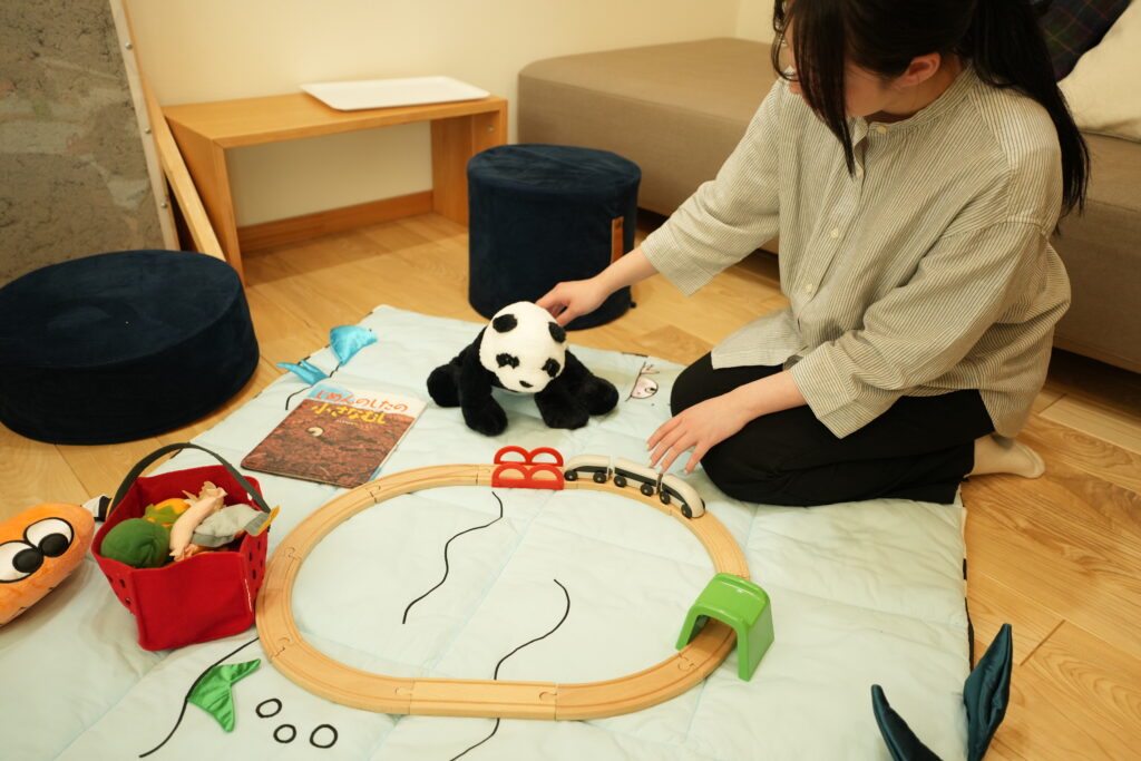 建築工房いろはが開催する注文住宅の完成見学会で、キッズスペースにて子守りスタッフが子どもと遊びながら家づくり相談中の家族をサポートする様子。