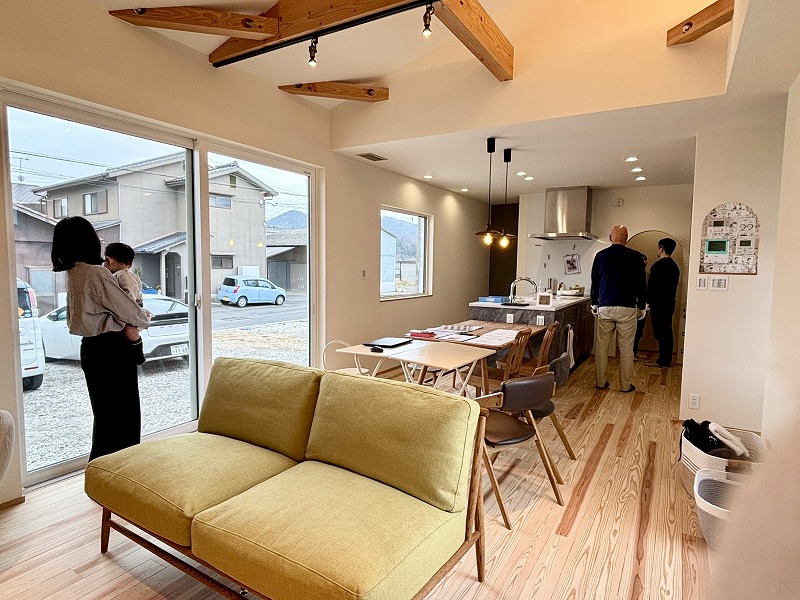 建築工房いろはが手掛けた注文住宅のLDKで、無垢床と梁あらわしのある明るい空間を来場者が見学している様子を写した写真で、家づくりや工務店選びの参考となる室内デザインが分かる内容です。
