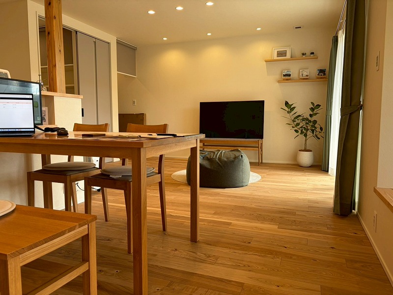 建築工房いろはが手掛けた注文住宅の施工例で、温かみのある無垢材のフローリングに木製のダイニングテーブルやテレビボードを配置し、ダウンライトの柔らかな光が室内を包み込む、ナチュラルで開放的なリビングダイニングの内観写真。