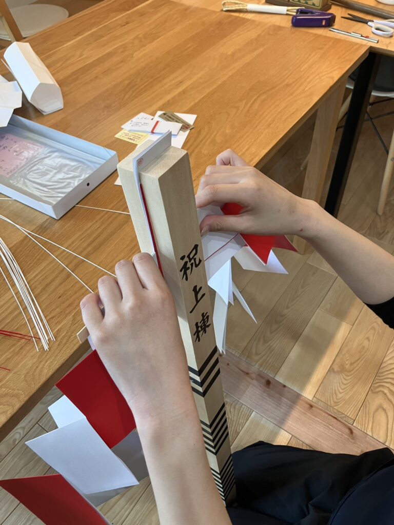 建築工房いろはのスタッフが「祝上棟」と書かれた幣束に赤と白の御幣を取り付けている、注文住宅の家づくりにおける上棟式の準備風景であり、施主様の安全と繁栄を願う工務店の丁寧な手仕事が伝わる一枚。