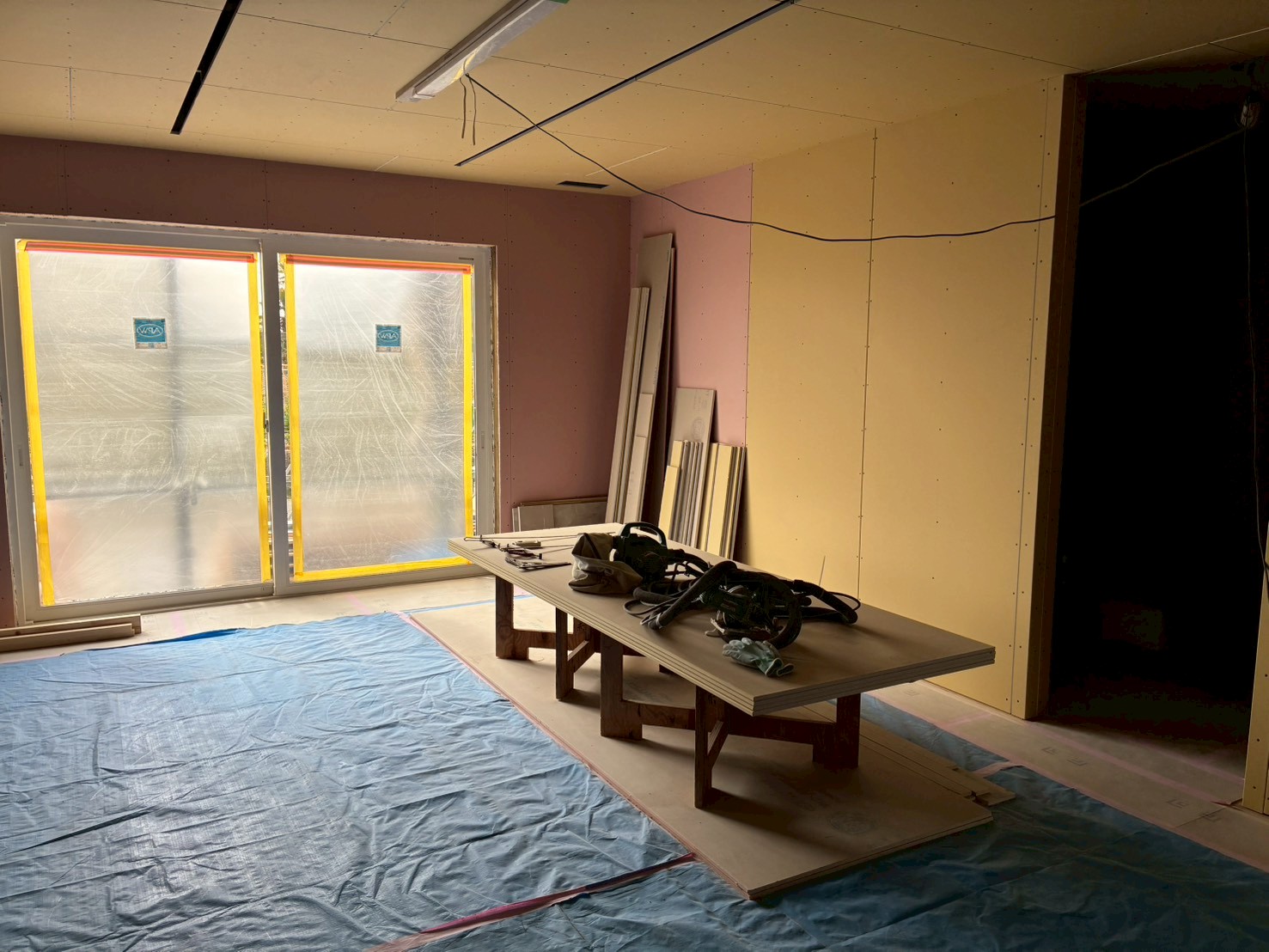 建築工房いろはが手掛ける注文住宅の建設現場において、石膏ボードの設置が完了し、ブルーシートでの養生や作業台、工具が整然と置かれた室内での家づくりの工程を記録した写真。