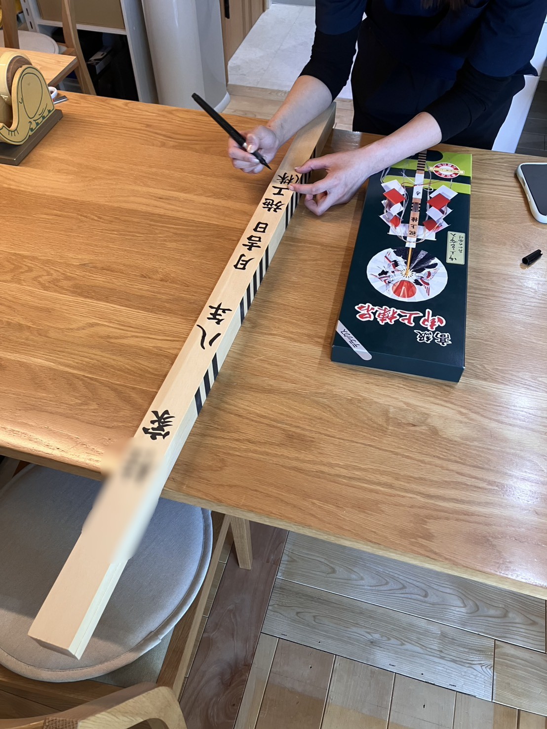 注文住宅の上棟式に向けて、建築工房いろはのスタッフが木製の幣串に建築日や施工会社名、施主名を筆ペンで丁寧に書き入れている、工務店による家づくりの準備風景を収めた写真。