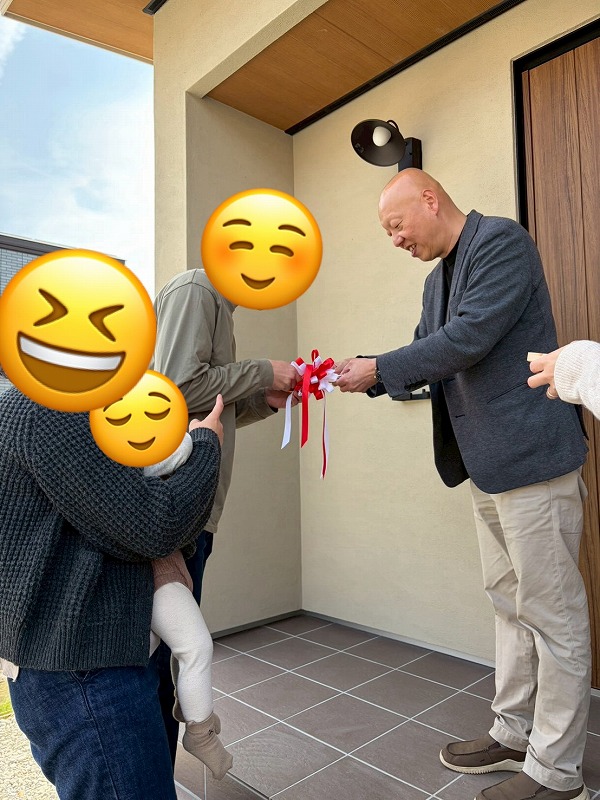 工務店の建築工房いろはが手掛けた注文住宅の引き渡しセレモニーにて、新築住宅の玄関ポーチで施主様とスタッフが笑顔でテープカットを行い、家づくりの節目を祝う感動的な瞬間を収めた写真です。