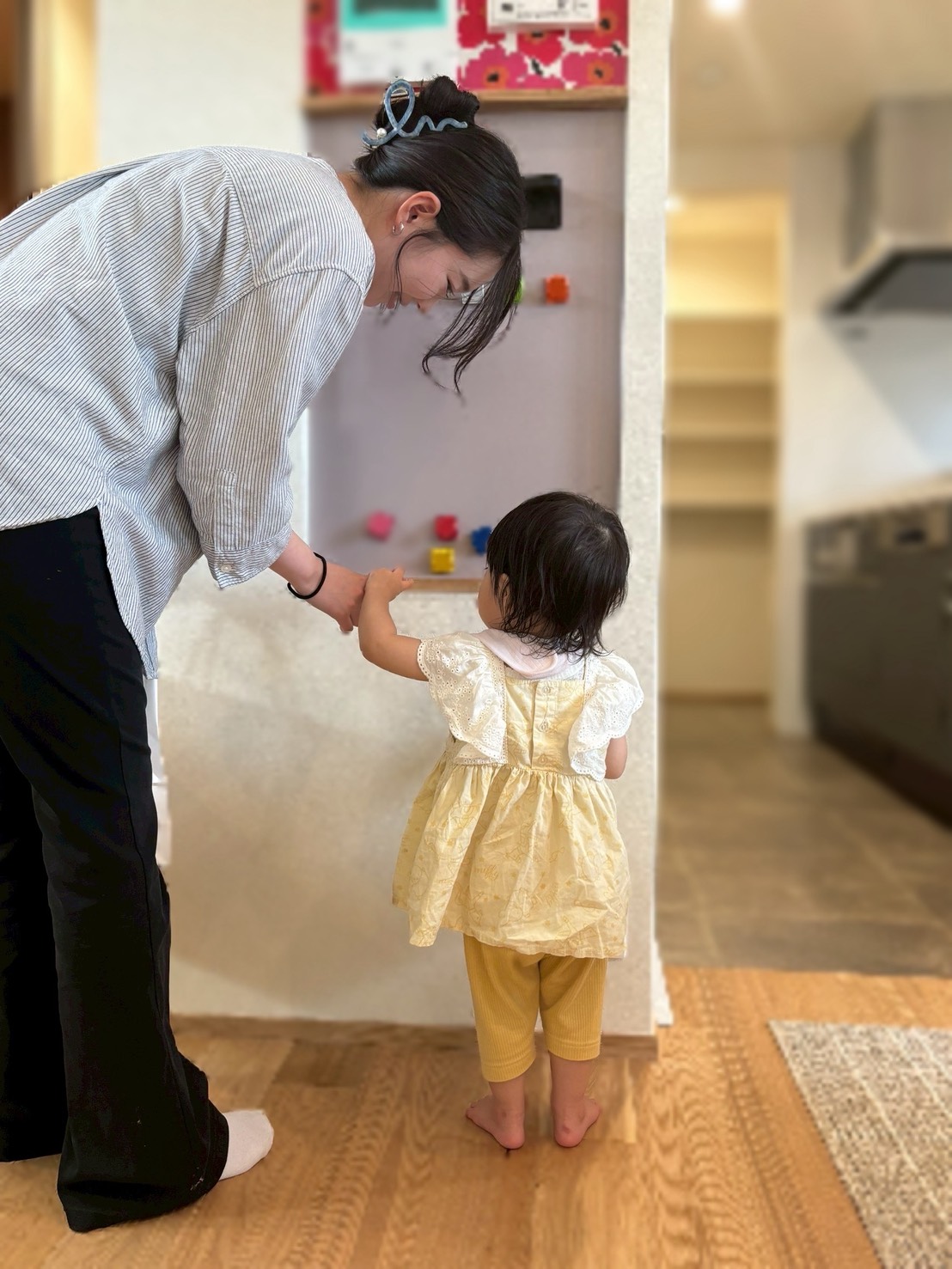 建築工房いろはが施工した注文住宅のリビングで、スタッフと幼い子供が無垢材フローリングの上に立ち、壁に設置されたマグネットボードで一緒に遊んでいる、子育て世代の理想的な家づくりの風景を捉えた写真。