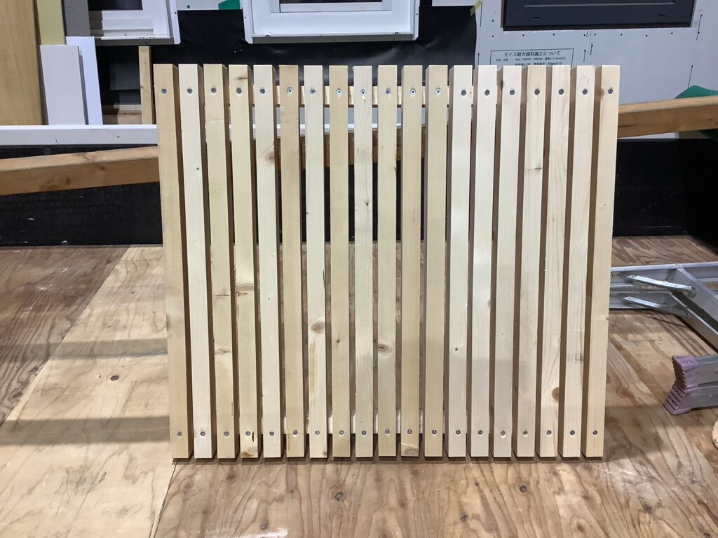 等間隔に並べられた白木の縦格子が、ビスでしっかりと固定されている施工中の様子。木の質感が活かされた造作部材が、建築現場の合板フロアの上に設置されています。