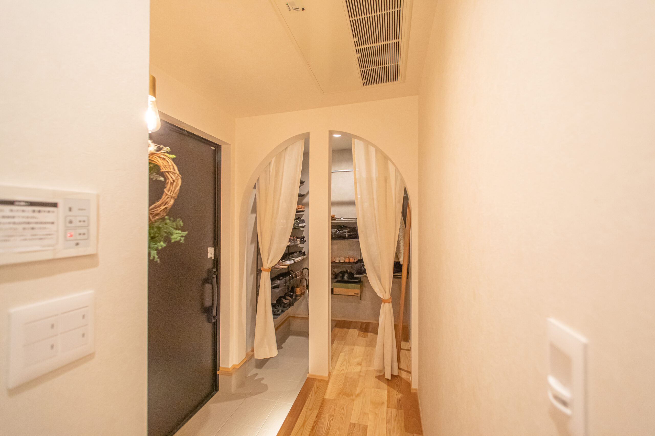 アーチ開口と柔らかなカーテンが印象的な、デザイン性の高いシューズクローク(土間収納)。玄関から続くフローリングと調和した温かみのある空間で、靴や小物をすっきりと隠しながら収納できる実用的な設計です。