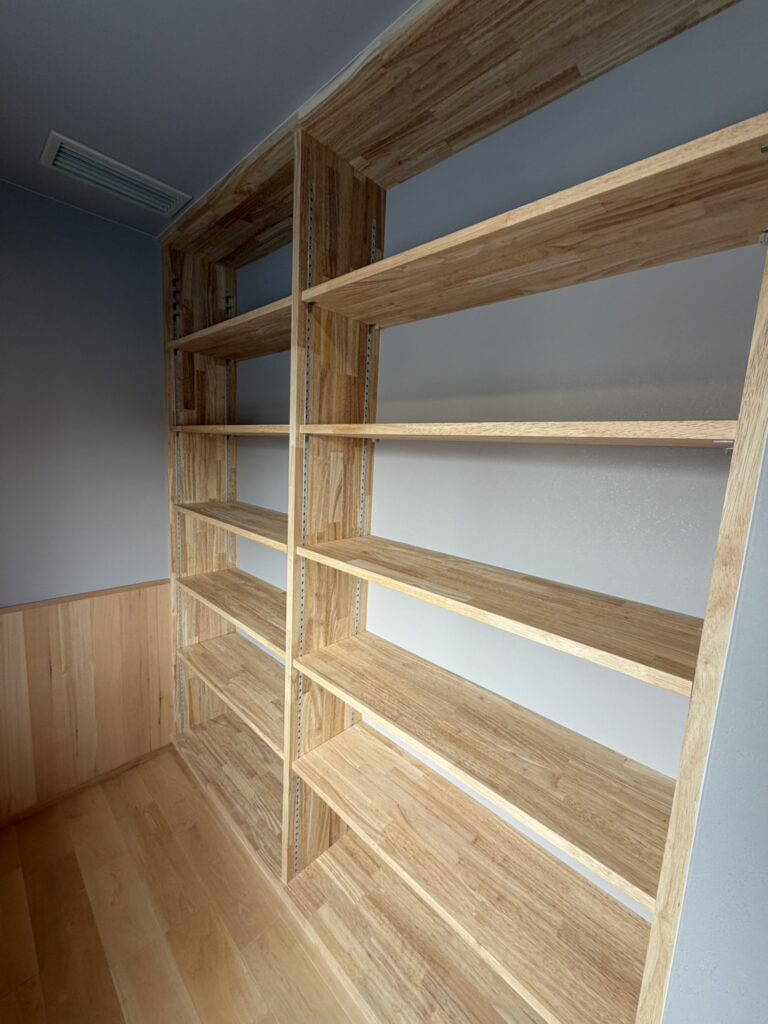 淡いブルーのアクセントクロスが爽やかな、ハンガーパイプと枕棚を備えたウォークインクローゼット。無垢材のフローリングと、アーチ状の垂れ壁による開口部が、空間に柔らかい印象と実用性を両立させています。