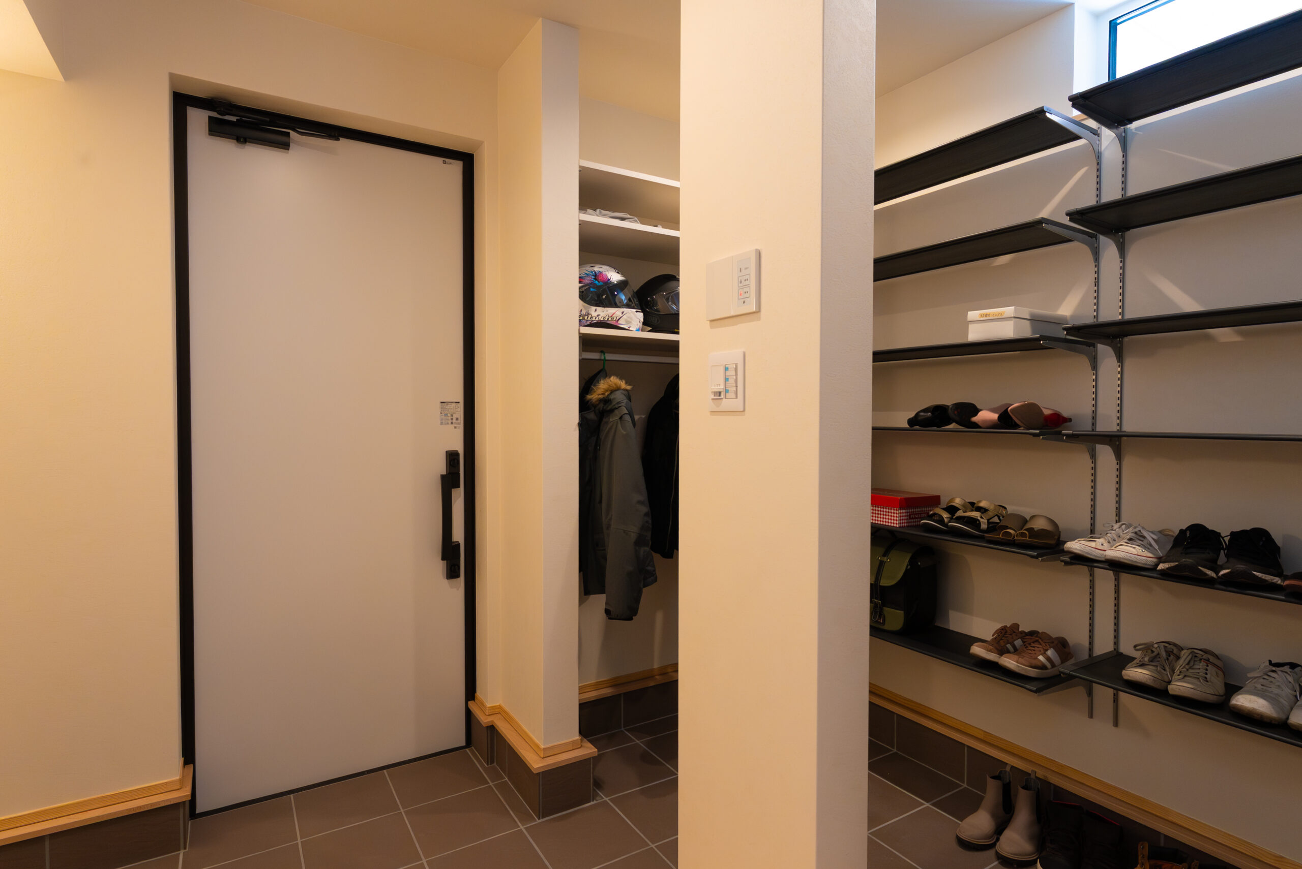 土間収納(シューズクローク)を備えた玄関の内観。可動棚には靴やヘルメットが整理され、ハンガーパイプにはアウターが掛けられるなど、機能的で収納力豊富な家事動線の良い設計です。