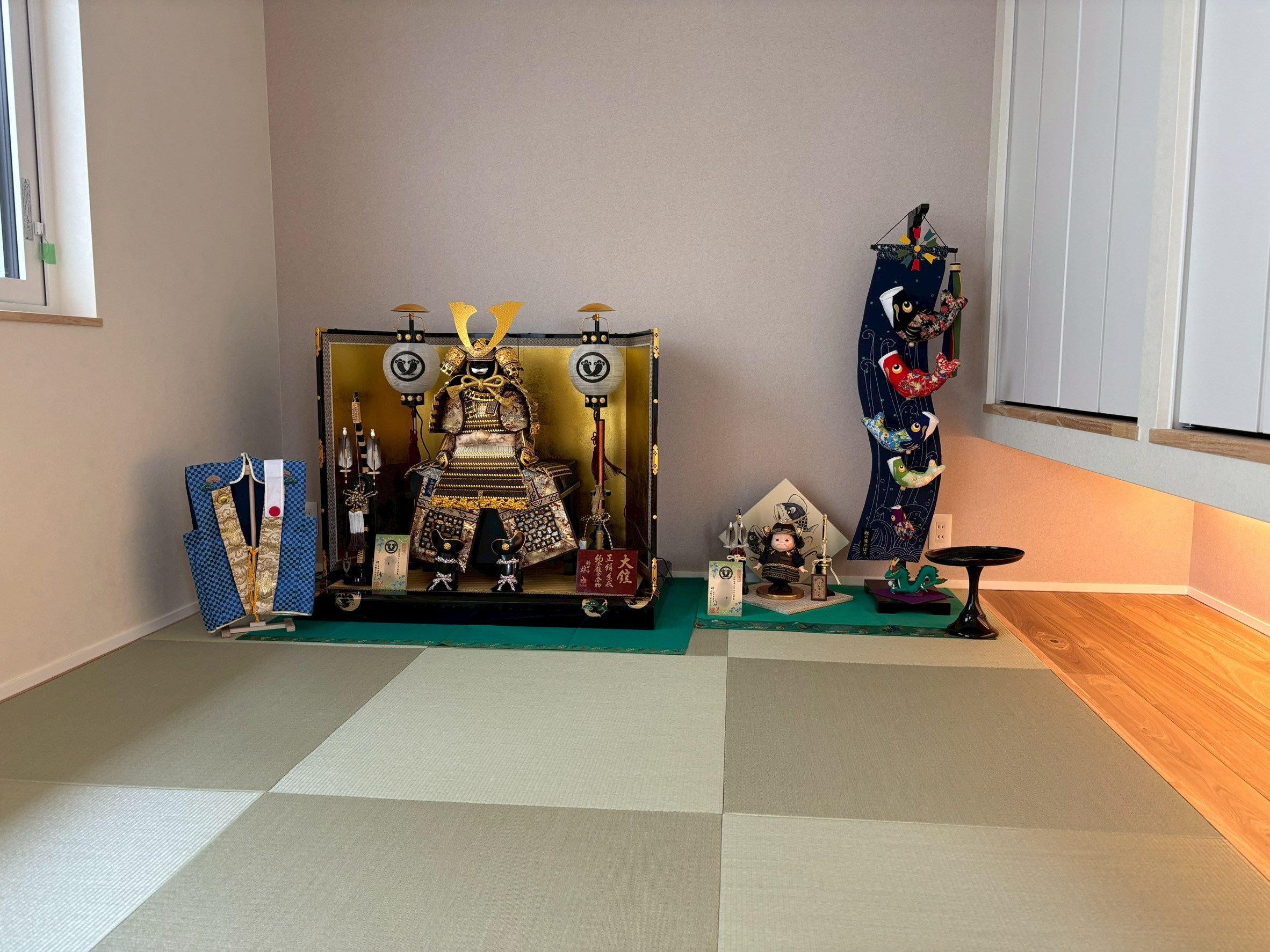 縁なしの半畳畳が敷かれたモダンな和室に飾られた五月人形と兜飾り。吊り収納下の間接照明が木の温もりを演出し、伝統行事を大切にしながら現代のライフスタイルに馴染む和のデザイン空間。