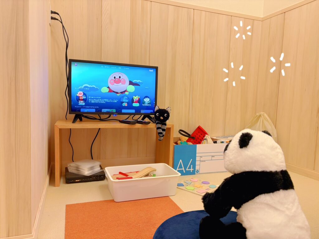 木の質感が心地よいナチュラルな板張りの壁に囲まれた、清潔感のあるキッズスペース。テレビではアニメが放映され、パンダのぬいぐるみや積み木、おもちゃ箱が備え付けられており、小さなお子様連れのご家族も打ち合わせに集中できる配慮の行き届いた空間です。