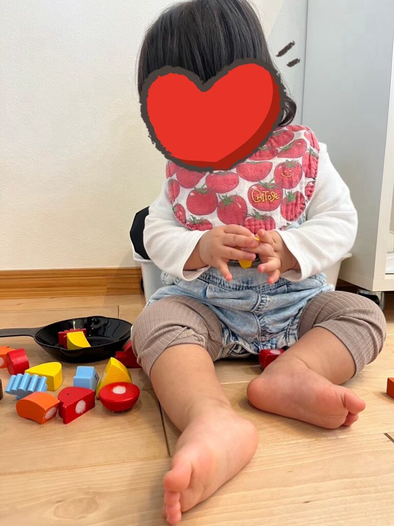 明るい木目調のフローリングで、カラフルな木のおもちゃや小さなフライパンを使っておままごとを楽しむお子様。お子様連れでも安心して遊べる、温かみのある快適な室内空間です。