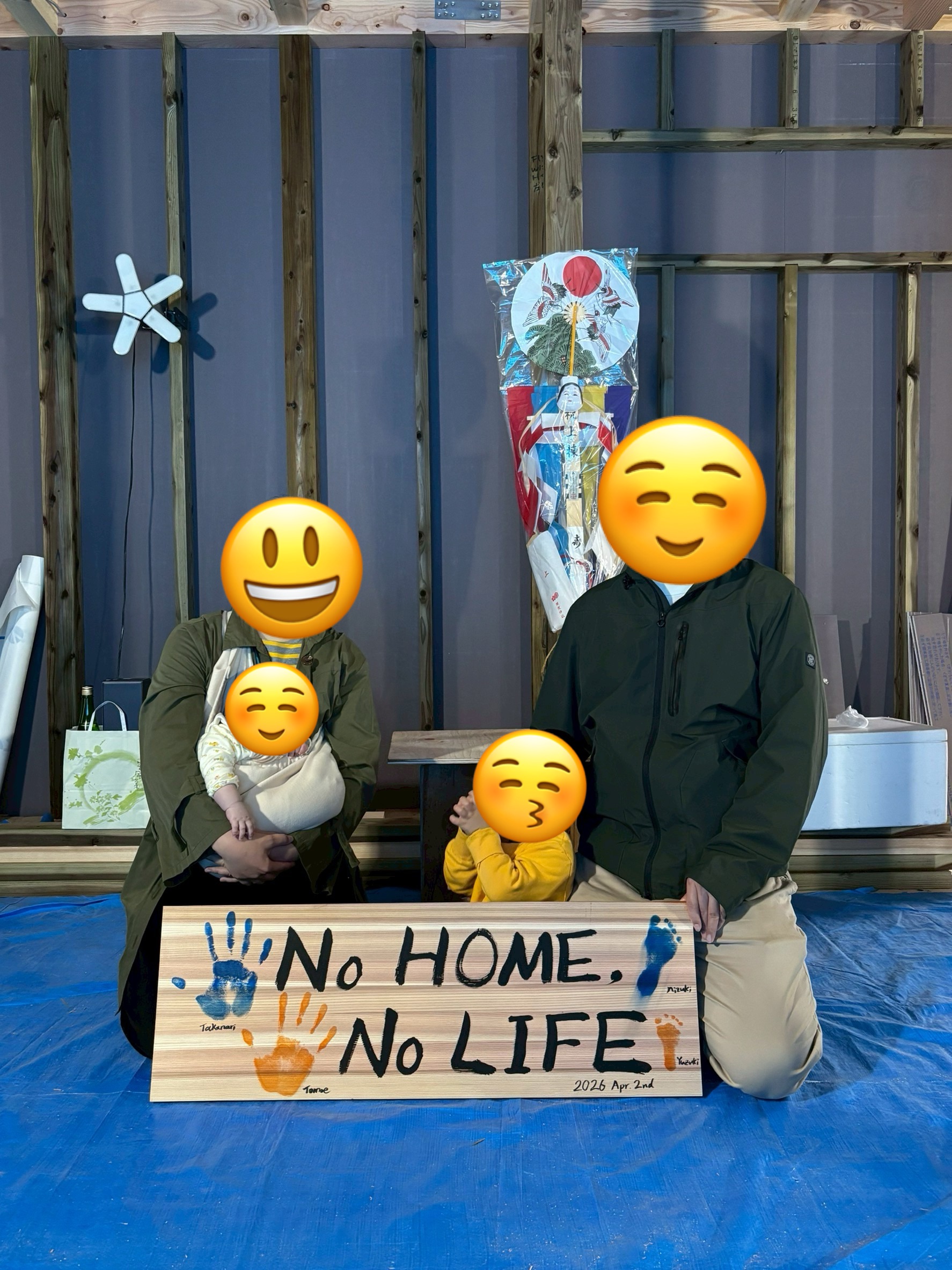 建築中の木造住宅の構造体を背景に、家族4人の手形・足形と「NO HOME, NO LIFE」というメッセージが描かれた記念板を囲む、上棟式や工事中の思い出を形にした家族写真。