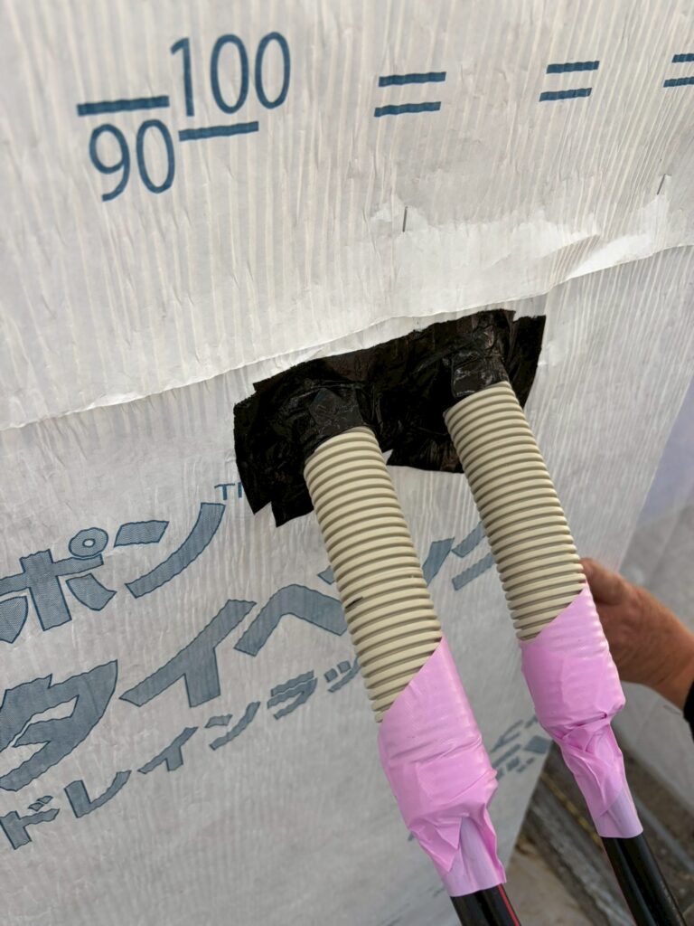 外壁の透湿防水シートから引き出された2本の配線保護管（CD管・PF管）の根元を、防水テープで隙間なく密着させた施工箇所。壁内への雨水浸入や漏水を防ぐ、徹底した防水・気密処理のディテールです。