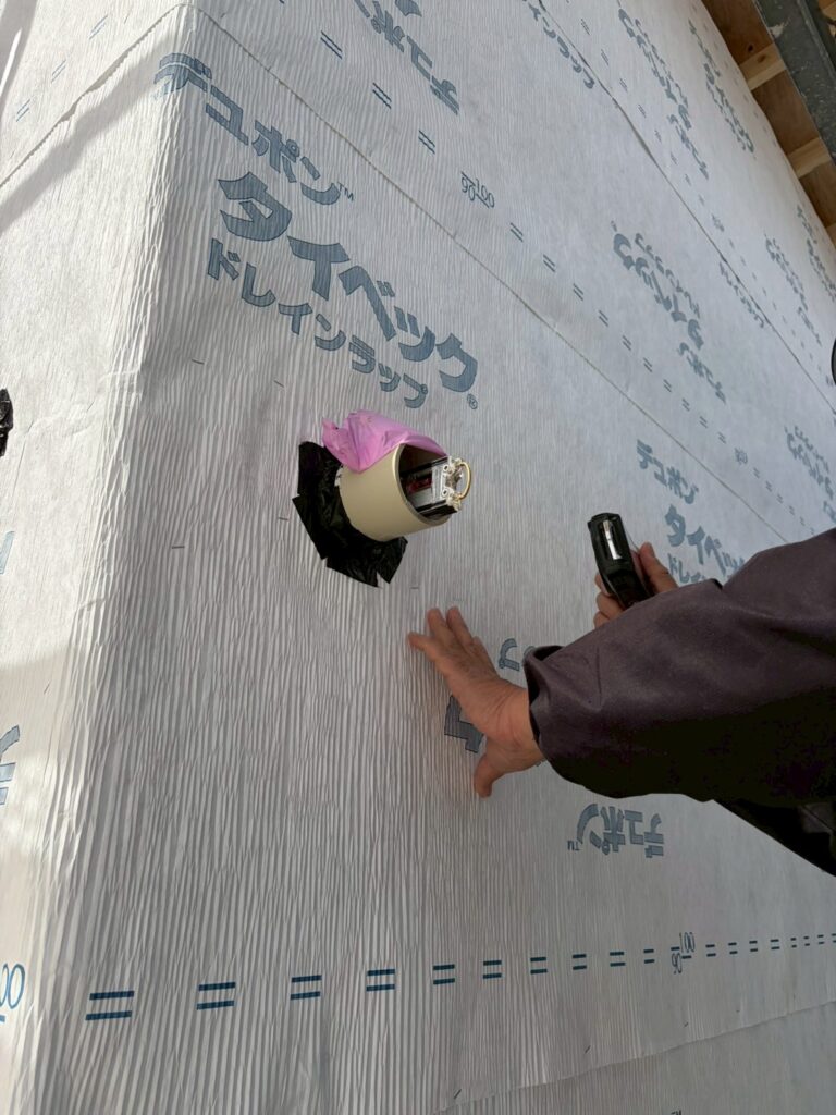 外壁の透湿防水シート「デュポン タイベック ドレインラップ」の施工において、配管貫通部を防水テープで厳重に処理している様子。雨水の侵入を防ぐための丁寧な気密・防水施工の工程を記録しています。