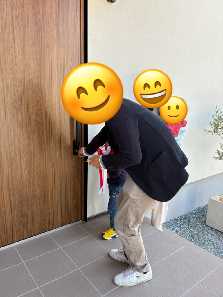 木目調の美しい玄関ドアに、初めて鍵を差し込んで開錠するお施主様ご家族。新しいマイホームでの豊かな暮らしが始まる、引き渡し式の感動的な瞬間。