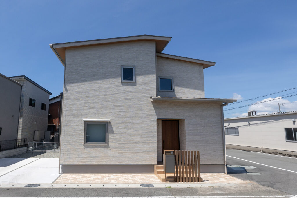 ベージュ系のタイル調外壁に、木目のアクセント格子が映えるシンプルでモダンな2階建て住宅。