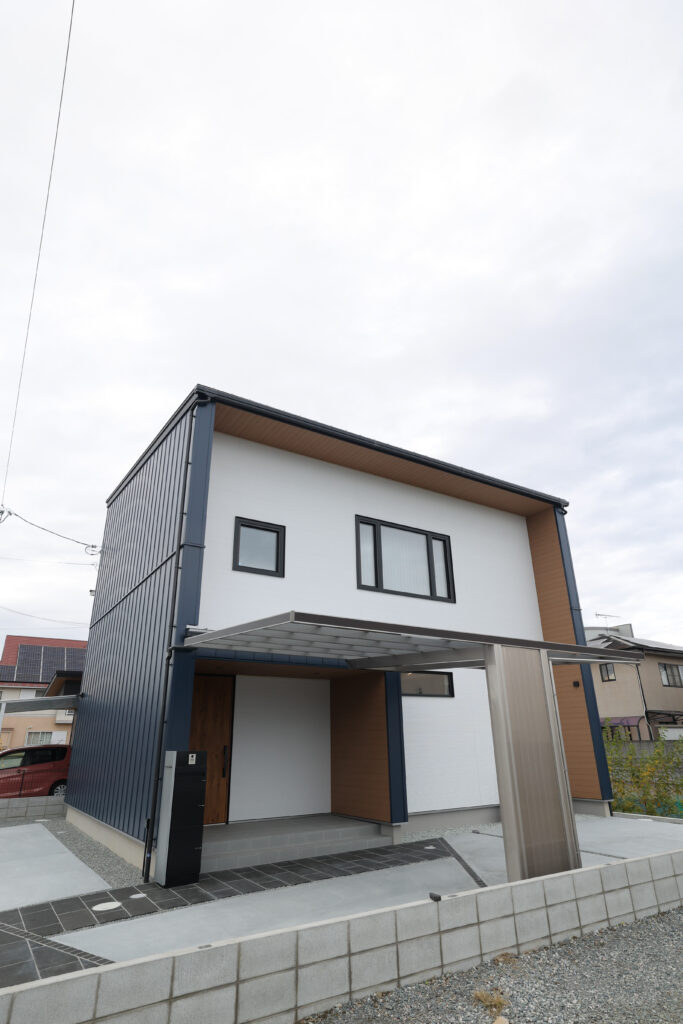 ネイビーのガルバリウム鋼板と白い外壁、木目調のアクセントが調和する、スタイリッシュでモダンな外観の2階建て住宅。