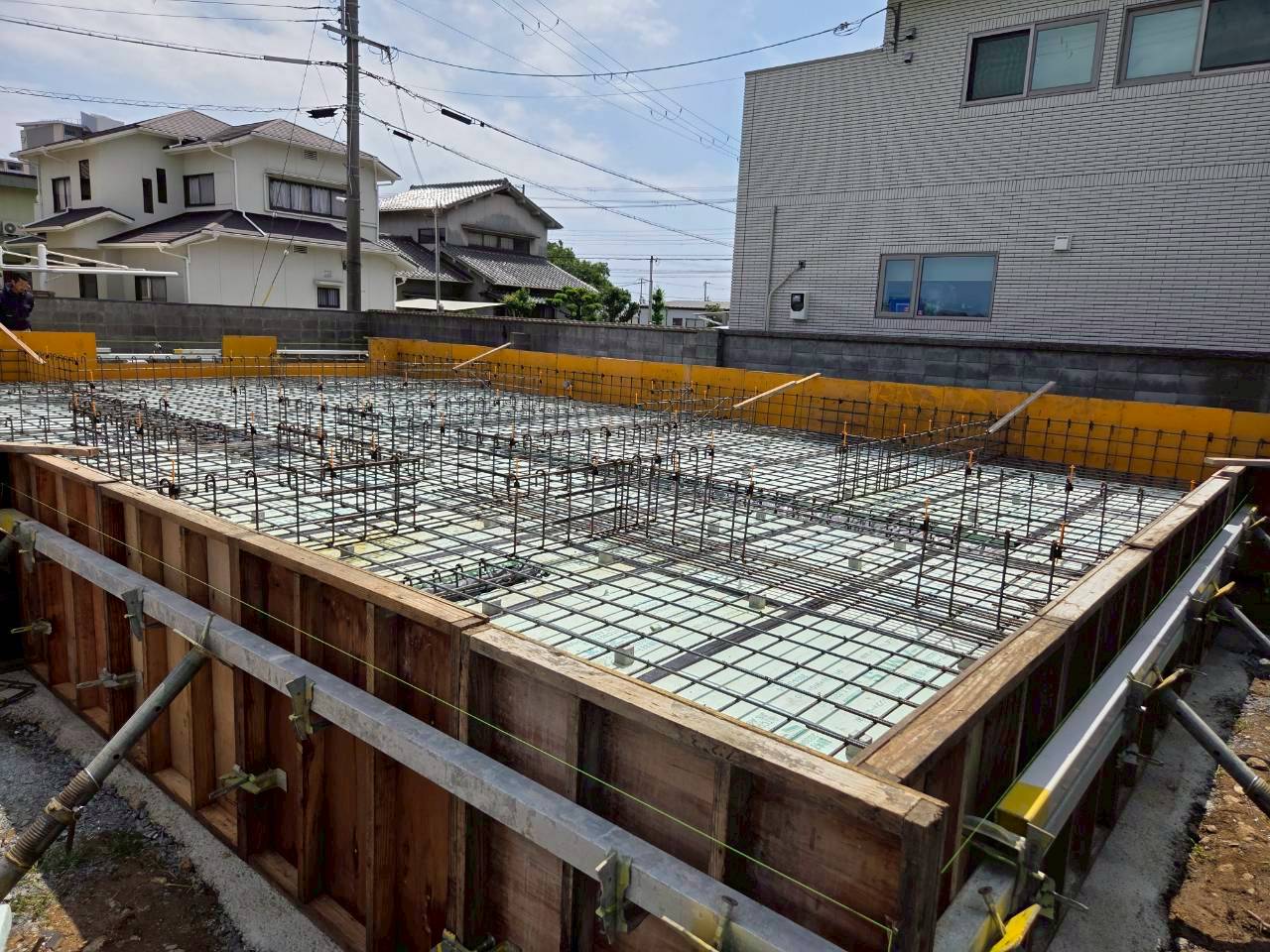 住宅の基礎工事現場にて、防湿シートと断熱材が敷かれた上に鉄筋が組まれ、施工の寸法精度を確認するためにスケールを当てて測定している様子。