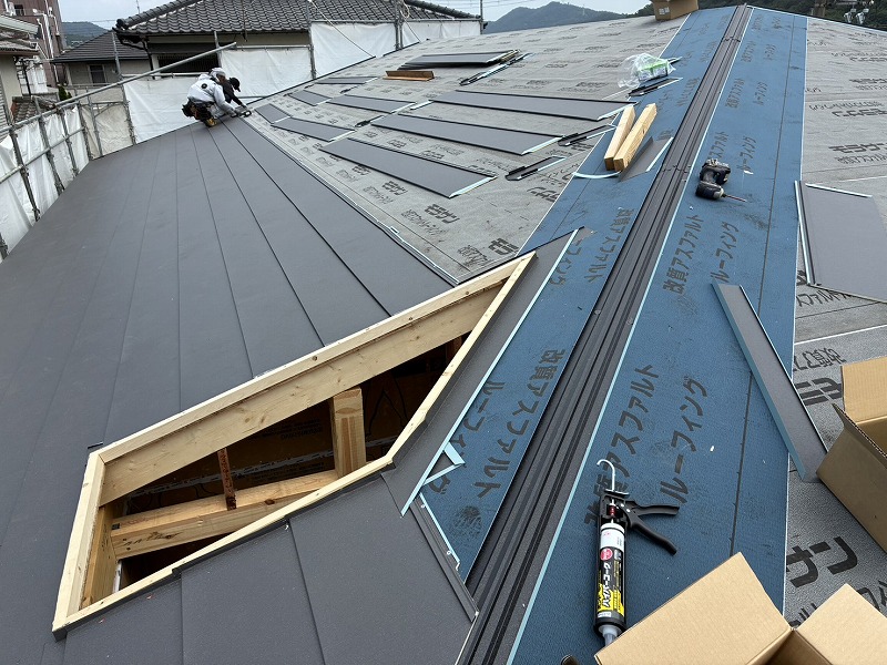 ガルバリウム鋼板の屋根とルーフィングシートが施工された上部に、木造の開口部が丁寧に収められている工事中の様子。