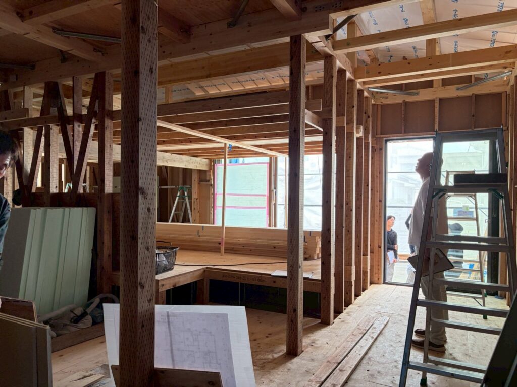 木造軸組工法で建てられた建築中の室内にて、柱や梁などの構造体が組み上げられた空間を確認している様子。