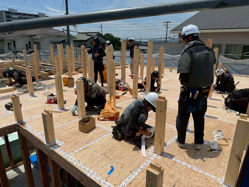 新築現場にて、職人たちが床合板の継ぎ目に気密テープを丁寧に貼付し、建物の気密性を高める施工を行っている様子。