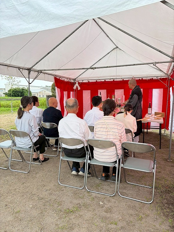 紅白の幕を張った地鎮祭のテント内で、祭壇に向かい神事の祝詞を聞く参列者たちの様子。