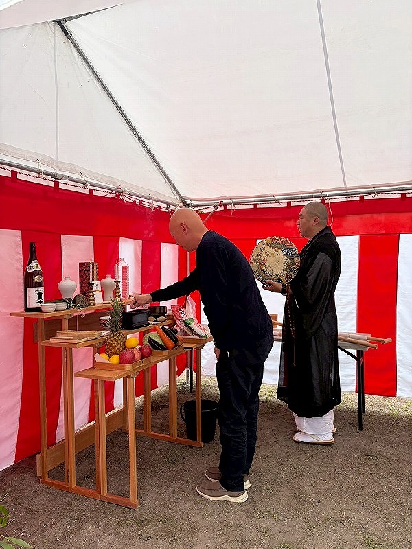 紅白の幕が張られたテント内で、祭壇にお供え物をし、僧侶が読経を行う地鎮祭の様子。