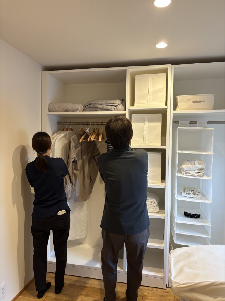 無垢材のフローリングが広がる寝室で、衣服を収納しやすいオープンタイプの可動式クローゼットを確認している様子。