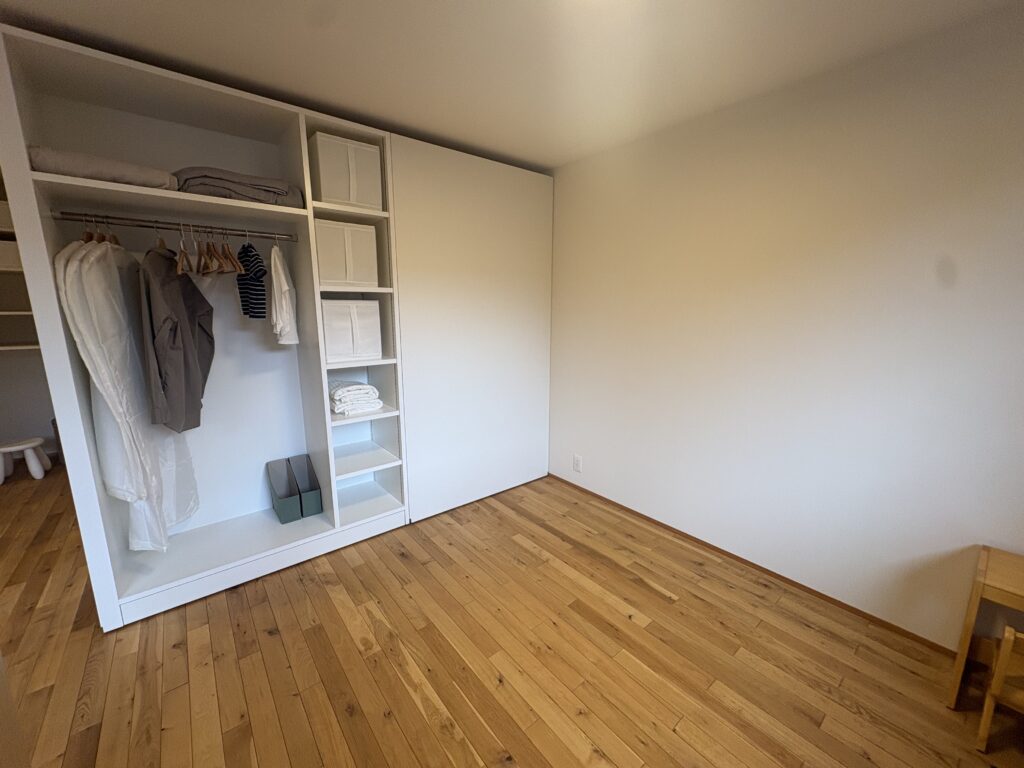無垢材のフローリングが心地よい寝室に、衣類を効率よく整理できる可動棚とハンガーパイプを備えた大容量のオープンクローゼット。