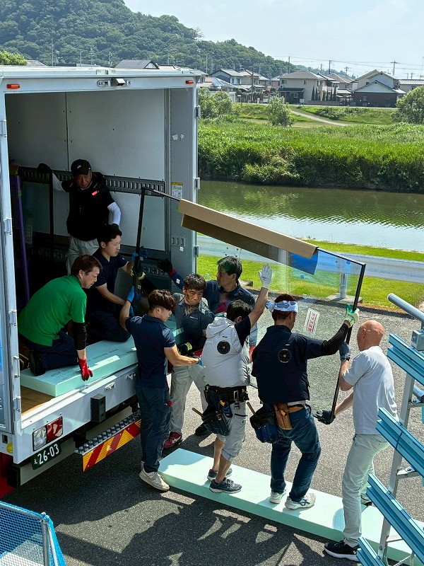 トラックの荷台から、スタッフたちがチームワークを活かして大開口の窓ガラスを慎重に搬入している様子。
