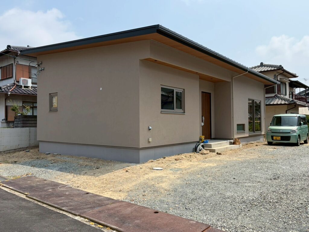 落ち着いた色合いの外壁に、木目の軒天と玄関ドアが調和するシンプルな平屋の住まい。