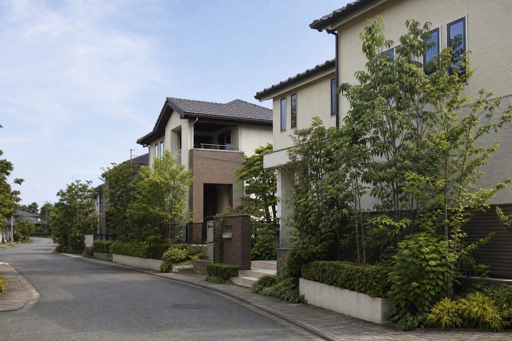 植栽の緑と調和した瓦屋根のモダンな戸建て住宅が連なる、落ち着きのある美しい住宅地の街並み。