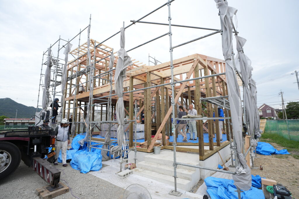 木造軸組工法による住宅の建て方工事が進み、足場と木材の構造躯体が組み上がった建築現場
