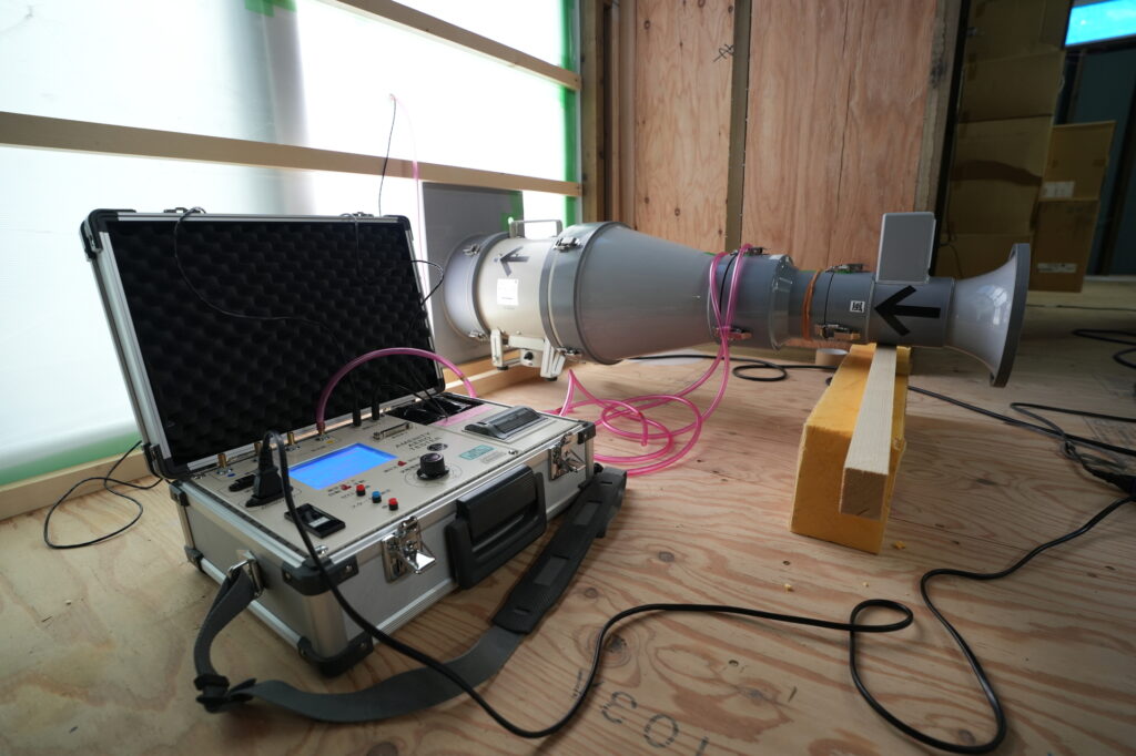 建築中の木造住宅の室内で、送風機と測定器を設置して高気密性能を測定する気密測定（C値測定）の機材