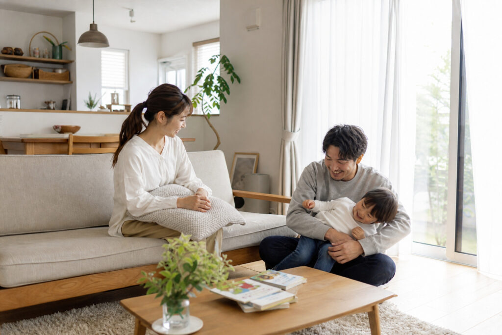 日当たりの良いリビングで、ソファとラグを囲みながら子どもと触れ合いくずろぐ3人家族の日常風景。