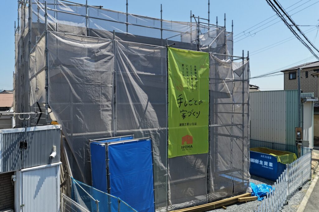 メッシュシートと足場で囲まれた新築工事現場に掲げられた、建築工房いろはのイメージシート