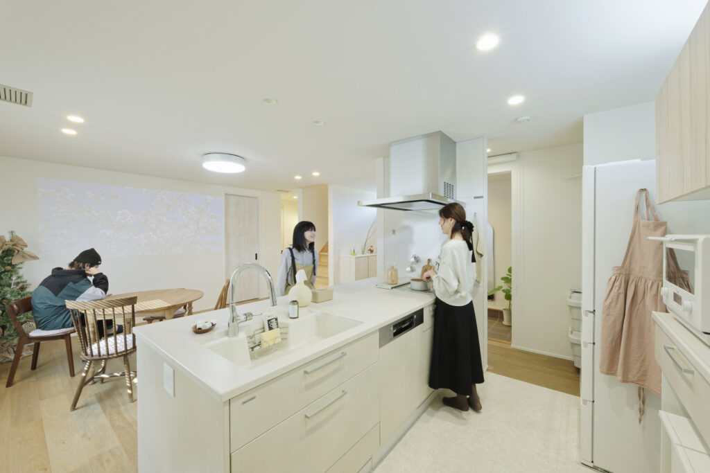 キッチンとダイニングで3人が料理や会話を楽しむ様子が写された家庭的な住まいの風景。