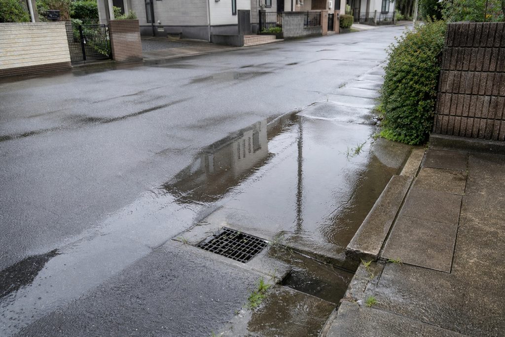 大雨の後に側溝や道路脇へ雨水が溜まり、街並みを映し出す住宅街の路面
