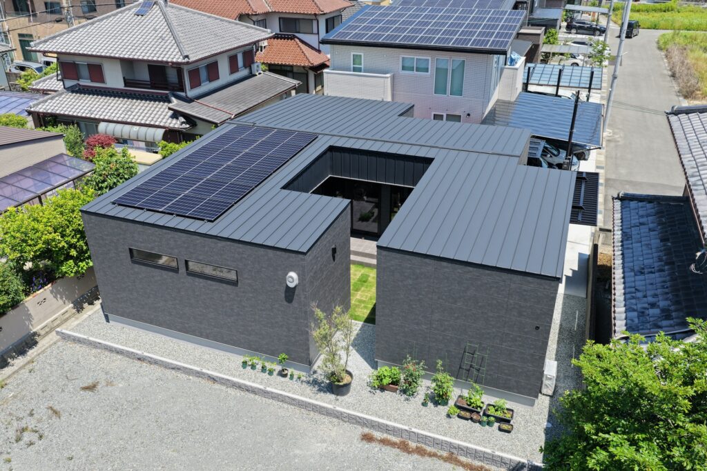 屋根に太陽光パネルを設置した黒いガルバリウム外壁の中庭付きコの字型平屋住宅