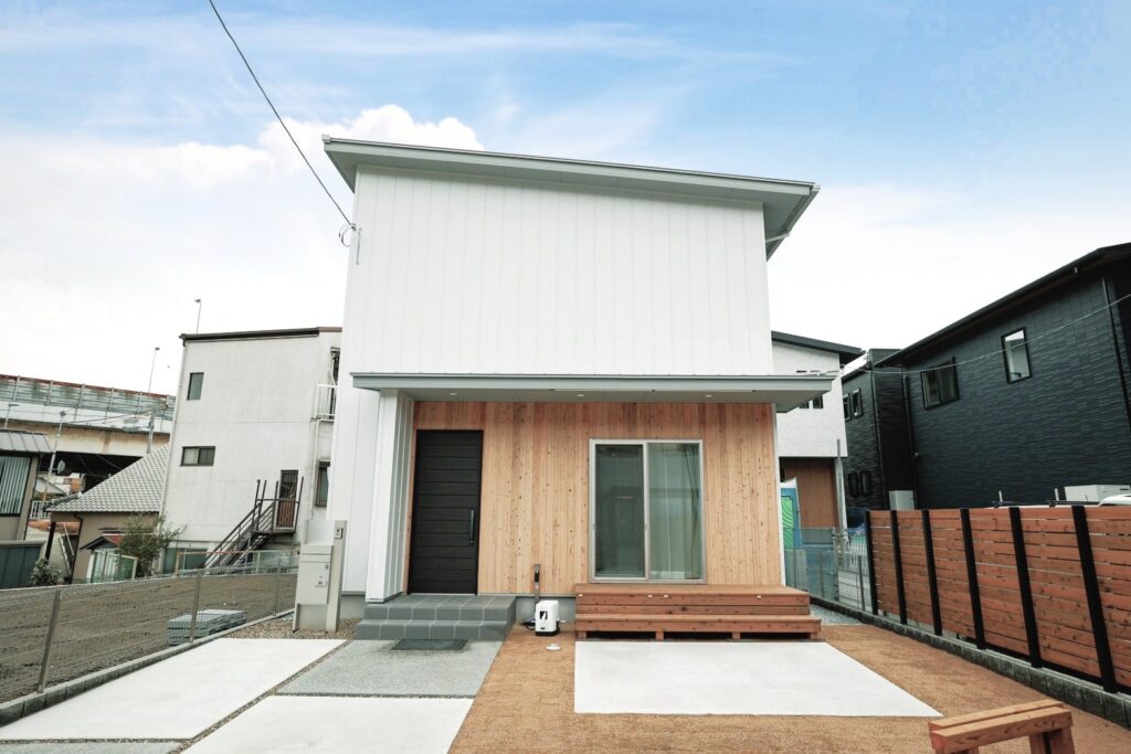 白い外壁と木目のアクセントが調和した二階建て住宅で、シンプルな外構とウッドデッキがあるモダンな外観デザイン。