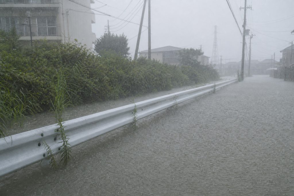 大雨により冠水し水没した住宅街の道路と、水面から突き出た白いガードレール