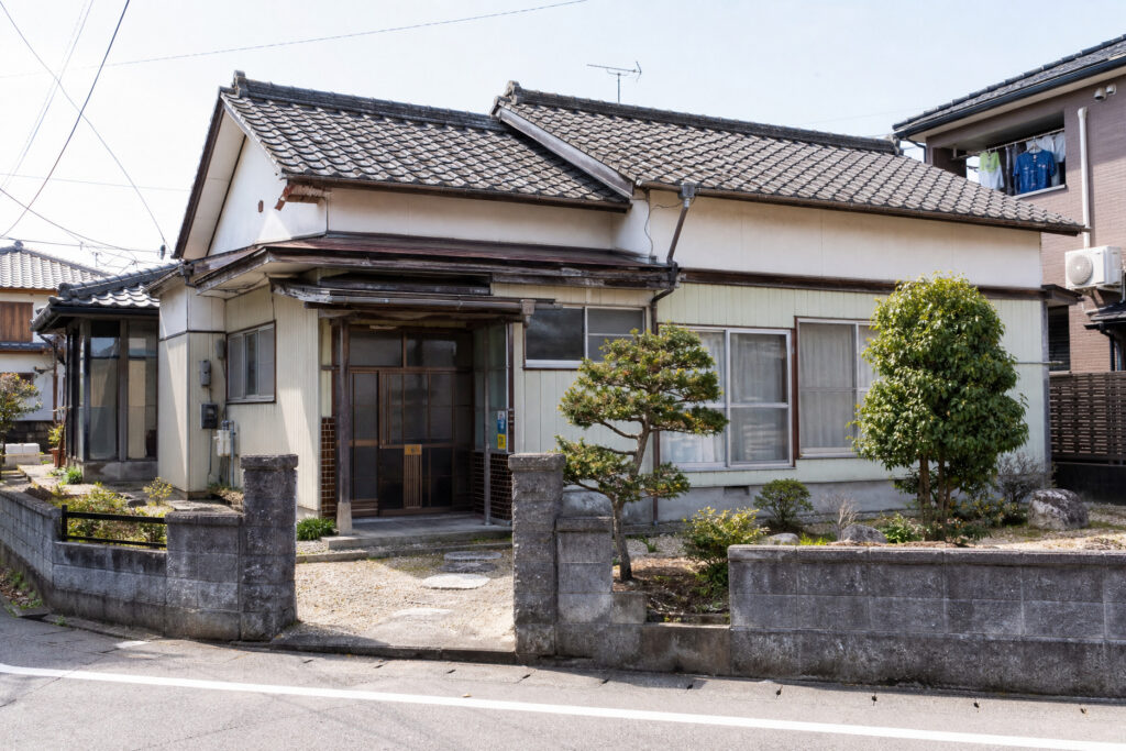 日本瓦の屋根や落ち着いた和風の佇まいと前庭の庭木が印象的な平屋建て木造住宅の建築外景写真。
