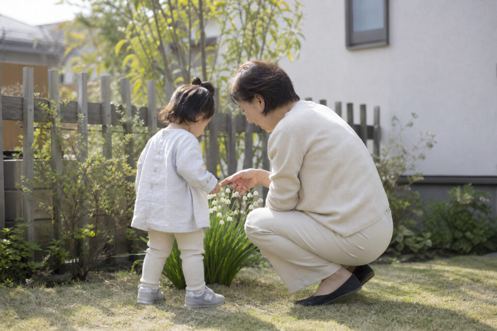 新築一戸建ての庭で小さな子供と大人が植物や花を観察しながら触れ合っている、家族の温かい暮らしや家づくりの魅力を表現した写真。
