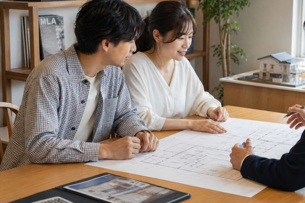住宅会社で図面を広げて家づくりの相談や打ち合わせを行う夫婦の写真。